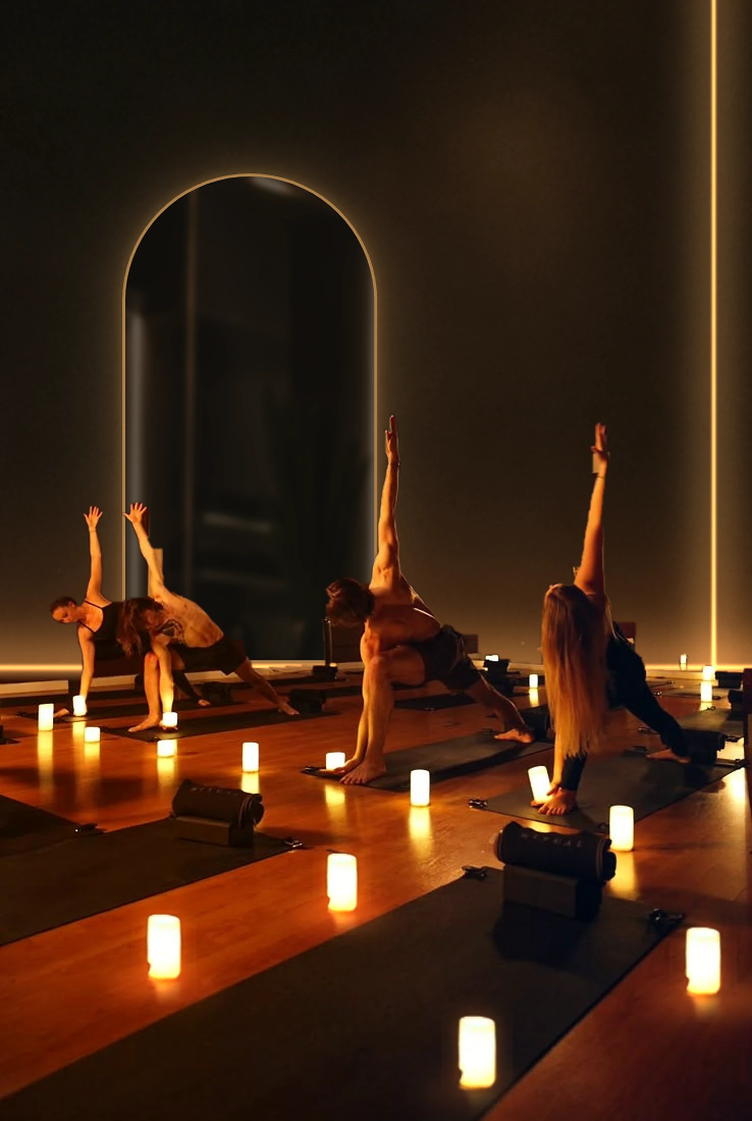 A small class holding a side-angle stretch on dark mats in a candlelit studio, warm light on one side and cool shadow on the other